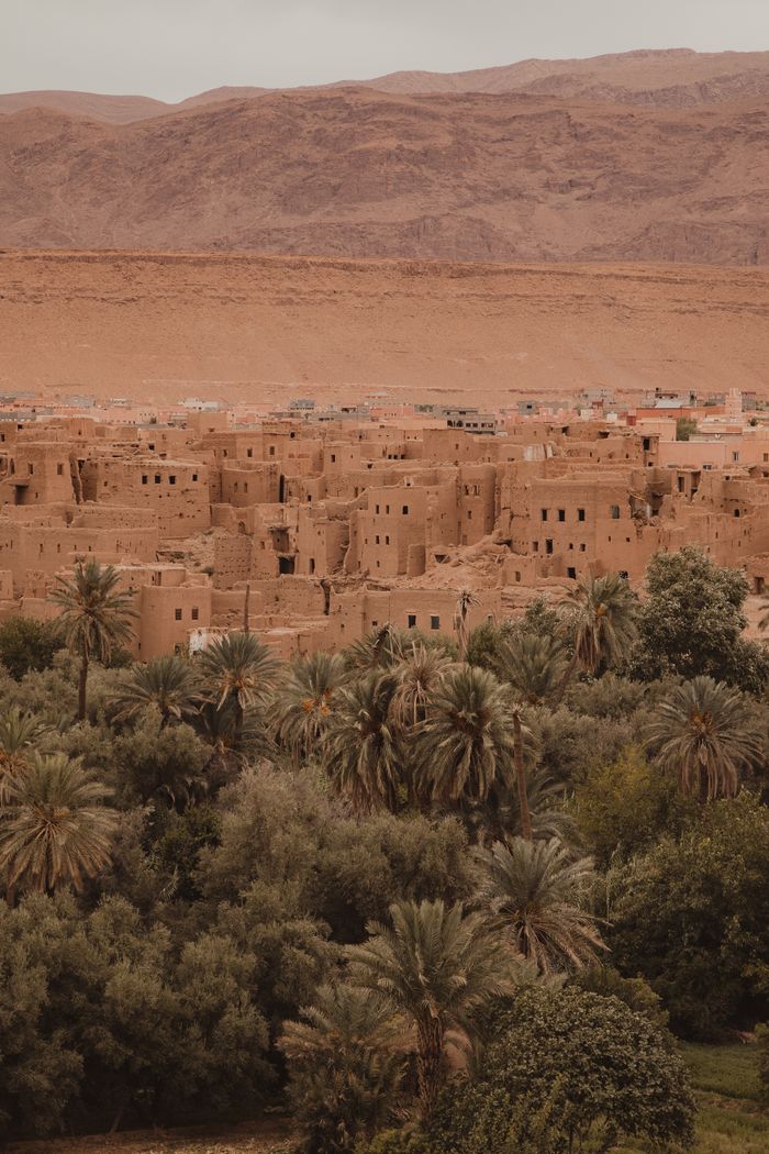 Home Aerial view of the historic Ait Ben Haddou in Morocco with surrounding desert and palm trees.