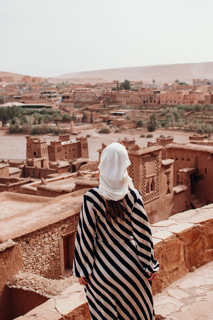 Services Woman in a striped dress and headscarf admiring Aït Benhaddou's desert architecture.