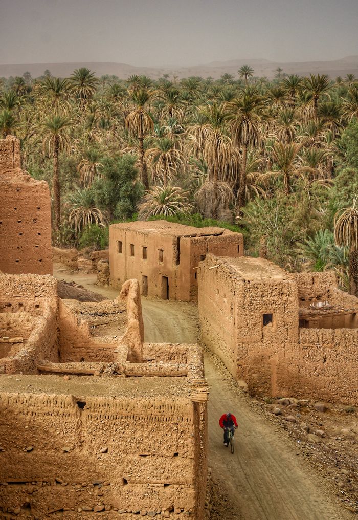 Crafting Captivating Headlines: Your awesome post title goes here A cyclist rides through a historic Moroccan village with clay buildings and lush palm trees.