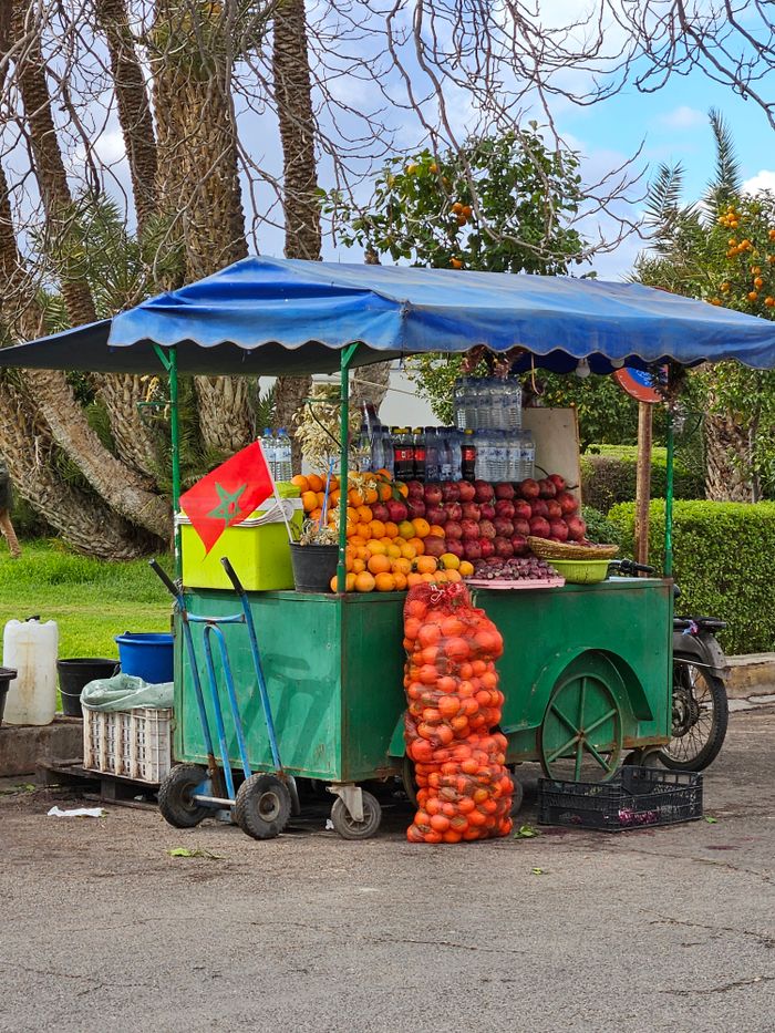 Vibrant street fruit cart in Marrakech with oranges and Moroccan flag under a blue canopy.